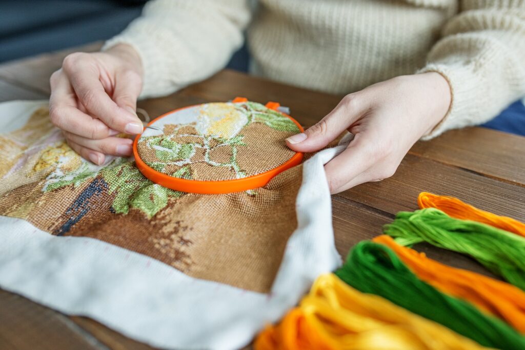 Making embroidery on canvas by women's hands in beige tones. Hobby and DIY concept